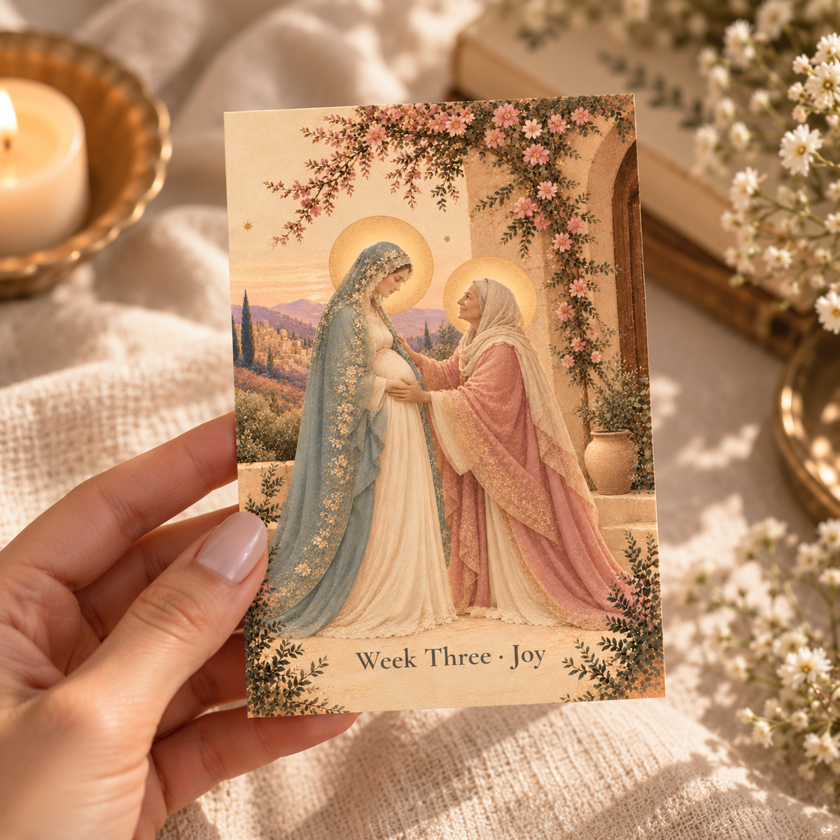 Hand holding a 4x6 Week Three Joy Advent prayer card of the Visitation by candlelight